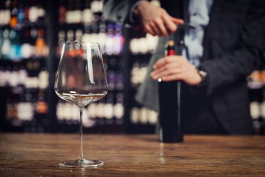 Sommelier 'in arka planındaki cam kadehi yakından incelerken tirbuşon şişe kırmızı şarapla açılıyor.