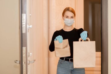Coronavirus salgını sırasında yiyecek teslimatı ve alışveriş. Eldivenlerde ve tıbbi maskelerde karton kutular tutan bir kız.