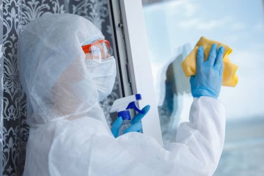 Koronavirüs salgını uyarısı yüzünden koruyucu biyolojik tehlike taşıyan bir kadın. Temizlik hizmeti dezenfektanları, böcek kontrol camları virüsten