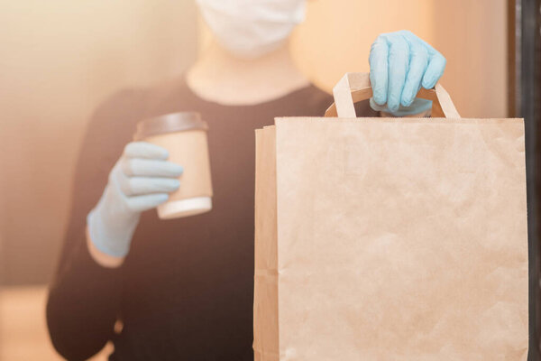 Delivery woman holding coffee and boxes cardboard in medical mask and rubber gloves. Quarantine online shopping