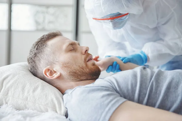 A biológiailag veszélyes állapotban lévő orvos ellenőrzi a karanténban lévő beteg pulzusát a coronavirus tünetei az ágyban — Stock Fotó
