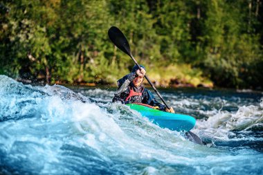 Ekstrem spor rafting beyaz su kayağı. Kanodaki adam dağ nehrine yelken açıyor.