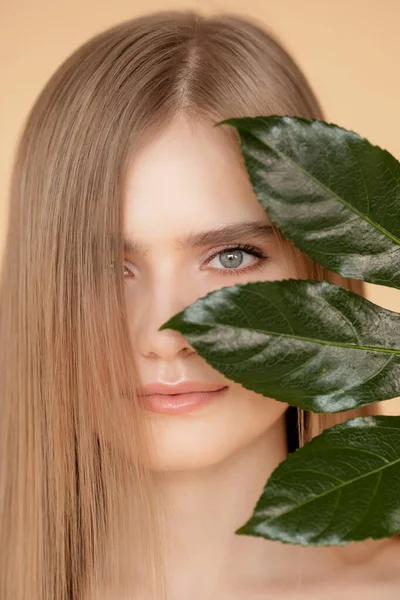 얼굴 피부, 눈썹, 머리카락을 위한 천연 화장품의 개념. 초록빛 잎을 가진 금발의 모델 소녀가 웃으면서 — 스톡 사진