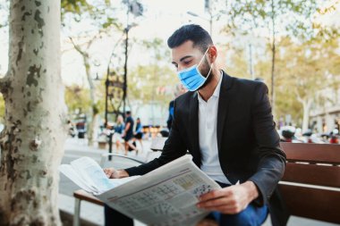 Bulaşıcı koronavirüse karşı yüz maskesi takan ve gazete okuyan bir adam.