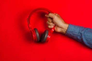 Kırmızı arka planda el ele tutuşan kırmızı kulaklıklar. Müzik konsepti