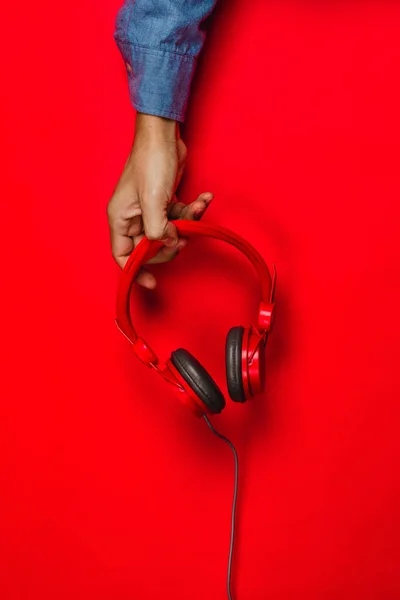 hand holding Red headphones on red background. Music concept