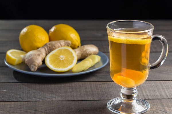 A cup of ginger tea with lemon on a wooden background.