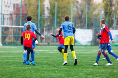 Kırmızı ve mavi spor giyimli çocuklar sahada futbol oynuyor, top sürüyor. Yeşil çimlerde top oynayan genç futbolcular. Eğitim, futbol, çocuk konsepti için aktif yaşam tarzı