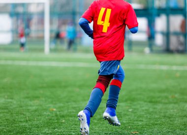 Kırmızı ve mavi spor giyimli çocuklar sahada futbol oynuyor, top sürüyor. Yeşil çimlerde top oynayan genç futbolcular. Eğitim, futbol, çocuk konsepti için aktif yaşam tarzı