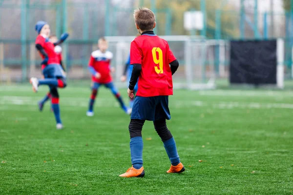赤と青のスポーツウェアの少年たちは フィールドにサッカー ドリブルボールを果たしている 緑の芝生の上でボールを持つ若いサッカー選手 トレーニング サッカー 子供のためのアクティブなライフスタイルの概念 — ストック写真