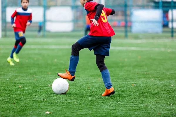Kırmızı ve mavi spor giyimli çocuklar sahada futbol oynuyor, top sürüyor. Yeşil çimlerde top oynayan genç futbolcular. Eğitim, futbol, çocuk konsepti için aktif yaşam tarzı