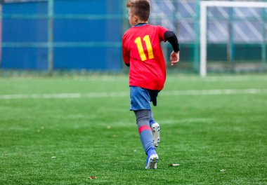 Kırmızı ve mavi spor giyimli çocuklar sahada futbol oynuyor, top sürüyor. Yeşil çimlerde top oynayan genç futbolcular. Eğitim, futbol, çocuk konsepti için aktif yaşam tarzı