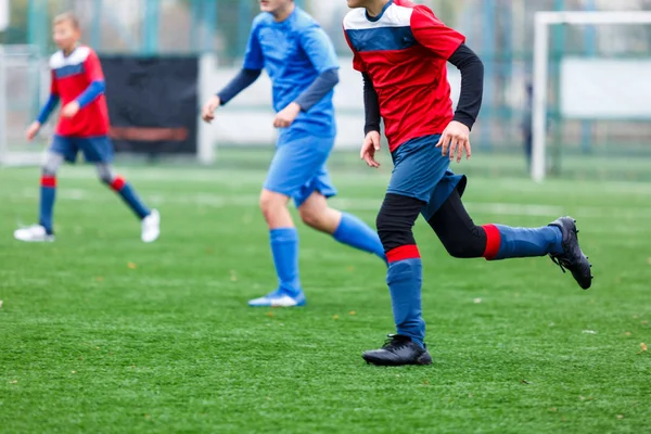 赤と青のスポーツウェアの少年たちは フィールドにサッカー ドリブルボールを果たしている 緑の芝生の上でボールを持つ若いサッカー選手 トレーニング サッカー 子供のためのアクティブなライフスタイルの概念 — ストック写真