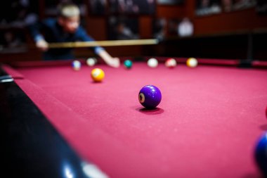 Boy plays billiard or pool in club. Young Kid learns to play snooker. Boy with billiard cue strikes the ball on table. Active Leisure, sport, hobby concept
