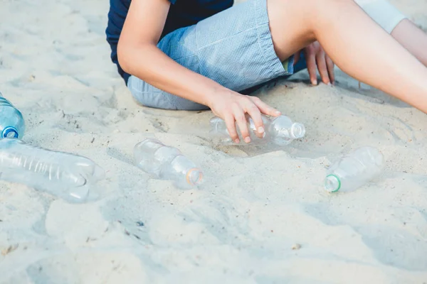 Volunteer boy in blue t shirt picks up dirty plastic bottles in park. Hands in yellow gloves collect garbage, pick up trash in bag. Eco activist cleaning up nature from plastic