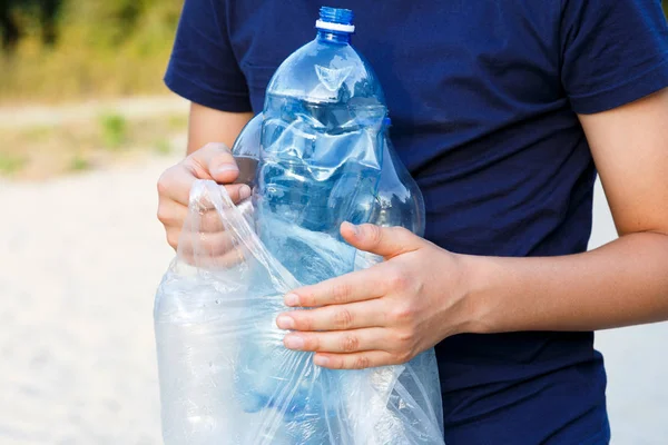 Volunteer boy in blue t shirt picks up dirty plastic bottles in park. Hands in yellow gloves collect garbage, pick up trash in bag. Eco activist cleaning up nature from plastic