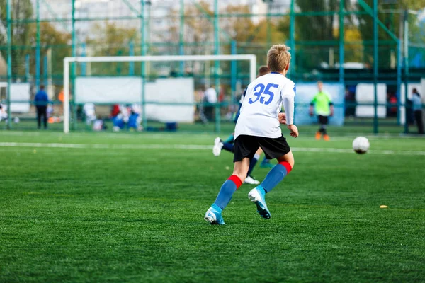 白と青のスポーツウェアを着た男の子は フィールドでサッカーをし ボールをドリブルします 緑の草の上にボールを持つ若いサッカー選手 トレーニング サッカー 子供のためのアクティブなライフスタイルコンセプト — ストック写真