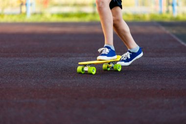 Sarı kaykaya binen mavi spor ayakkabılarla bacaklarını kapat. Aktif şehir yaşam tarzı gençlik, eğitim, hobi, aktivite konsepti. Çocuklar için açık hava sporu. Çocuk kaykayı.