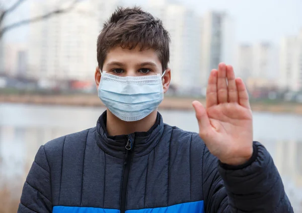 顔を手でカメラを見て上の保護医療用マスクの若い男の子 看板を停止します ウイルスの拡散に対してマスクでかわいいティーンエイジャーの屋外 大気汚染 ウイルス パンデミックコロナウイルス — ストック写真