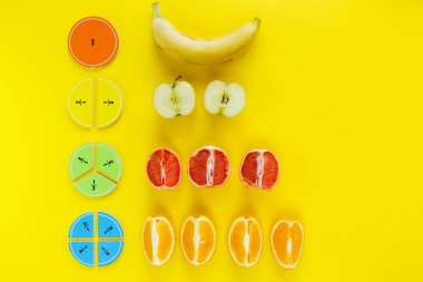 Renkli matematik kesirleri ve elmalar, portakallar, muz sarı arkaplan ya da masa üzerinde bir örnek olarak. Çocuklar için ilginç bir matematik. Eğitim, okul konseptine geri dönelim. Geometri ve matematik materyalleri.