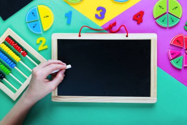 Çocuk okul yönetim kurulunda sol elle yazıyor. Renkli matematik kesirleri ve yeşil, sarı, mor arka planda kara tahta. Çocuklar için ilginç, eğlenceli matematik. Eğitim, okula dönüş konsepti.