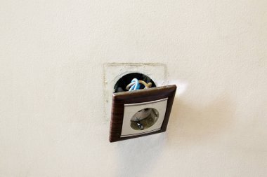 Duvardan kahverengi kırık elektrik prizi düştü. Priz duvardan sökülmüş. Elektrik güvenliği ihlali, elektrik şoku riski