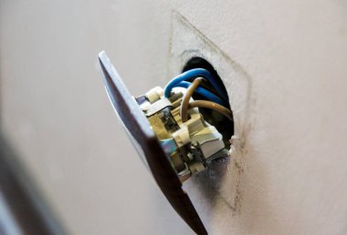 Duvardan kahverengi kırık elektrik prizi düştü. Priz duvardan sökülmüş. Elektrik güvenliği ihlali, elektrik şoku riski