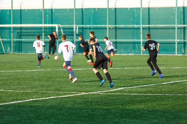 Boys in white black sportswear running on soccer field. Young footballers dribble and kick football ball in game. Training, active lifestyle, sport, children activity concept