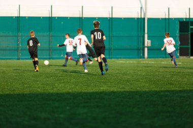 Futbol sahasında koşan beyaz takım elbiseli çocuklar. Genç futbolcular maçta top sürüp tekmeliyorlar. Eğitim, aktif yaşam tarzı, spor, çocuk aktivitesi konsepti