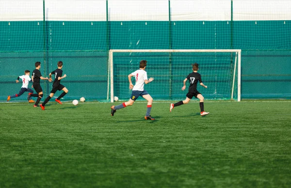 サッカー場を走る白黒のスポーツウェアを着た少年たち 若いサッカー選手は試合でサッカーボールをドリブルしてキックする トレーニング アクティブライフスタイル スポーツ 子供の活動のコンセプト — ストック写真