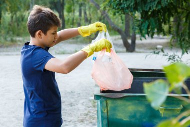 Eldivenli mavi tişörtlü çocuk çöpleri ve plastik şişeleri plajda paketlere doldurup konteynıra atıyor. Genç gönüllü. Çevre koruma, çevre konseptini kaydet