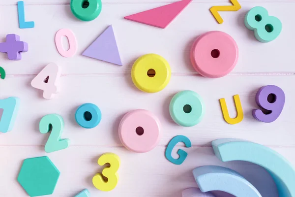 Wooden toy rainbow, numbers, blocks, pastel color arc on pink background. Natural no plastic toys for creativity development. Flat lay, top view. Educational games for kindergarten, preschool kids