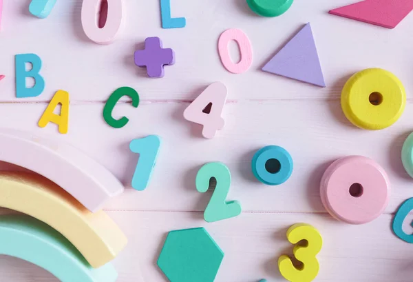 Wooden toy rainbow, numbers, blocks, pastel color arc on pink background. Natural no plastic toys for creativity development. Flat lay, top view. Educational games for kindergarten, preschool kids