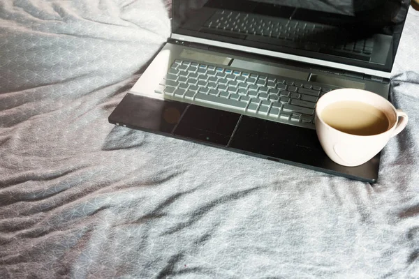 Close up of laptop and cup of coffee in the bed. Workspace for freelance, lifestyle. Distance work, online working, freelance concept.