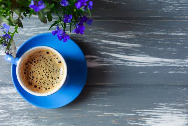 Gri ahşap masanın üzerinde küçük mavi bir fincan kahve ve badem kurabiyesi. Tencerede mavi bir çiçekle güzel bir yaz geçmişi var. Bahar kartı şablonu. Güzel, rahat bir sabah konsepti. Bahar, yaz mevsimi. Boşluğu kopyala
