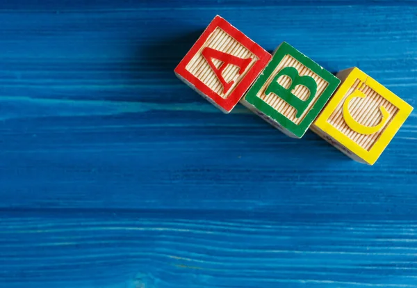 Multicolored wooden cubes with letters on blue background. Set for studying alphabet. Education, back to school concept. Top view, copy space