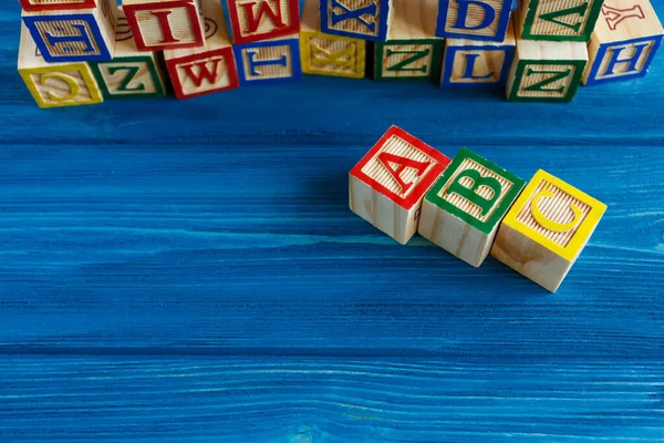 Multicolored wooden cubes with letters on blue background. Set for studying alphabet. Education, back to school concept. Top view, copy space