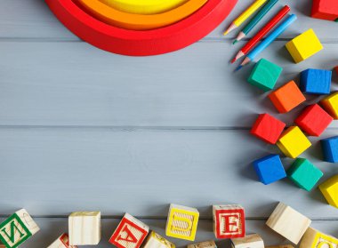 Çok renkli tahta küpleri harflerle, kalemlerle, gri arka planda gökkuşağı kavisleriyle kapatın. Alfabe çalışmak için oyuncak seti. Eğitim, okul konseptine geri dönelim. Üst görünüm, alanı kopyala