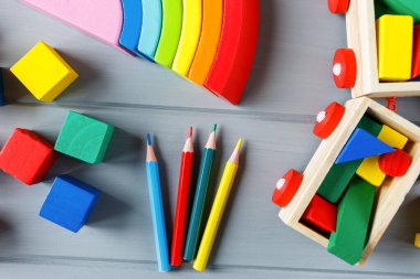 Çok renkli tahta küpleri harflerle, kalemlerle, gri arka planda gökkuşağı kavisleriyle kapatın. Alfabe çalışmak için oyuncak seti. Eğitim, okul konseptine geri dönelim. Üst görünüm, alanı kopyala