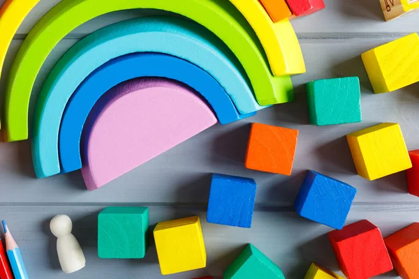 Çok renkli tahta küpleri harflerle, kalemlerle, gri arka planda gökkuşağı kavisleriyle kapatın. Alfabe çalışmak için oyuncak seti. Eğitim, okul konseptine geri dönelim. Üst görünüm, alanı kopyala