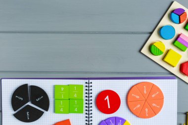 Gri ahşap masadaki açık not defterindeki çok renkli matematik kesirlerini kapat. Çocuklar için ilginç bir matematik. Eğitim, okula dönüş konsepti.