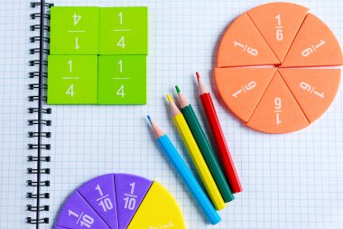 Gri ahşap masadaki açık not defterindeki çok renkli matematik kesirlerini kapat. Çocuklar için ilginç bir matematik. Eğitim, okula dönüş konsepti.
