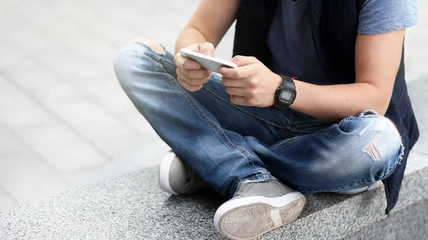 一个年轻人坐在柏油路上使用智能手机. — 图库照片