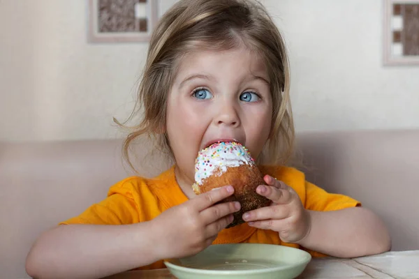 Um bebé giro está sentado à mesa a comer um pão. Criança com olhos azuis — Fotografia de Stock