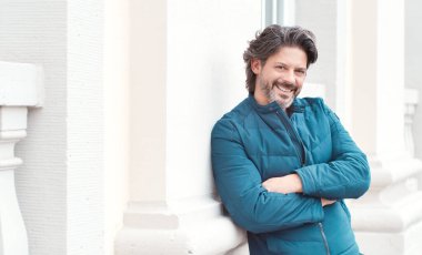 Kollarını kavuşturup kameraya bakan gülümseyen adam.