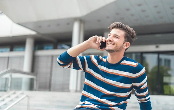 Young cheerful man holding mobile phone, using smartphone, making a call — Stock Photo, Image