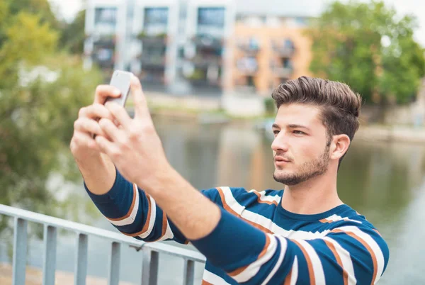 Compartiendo autofoto feliz. Hermoso hombre sonriente en ropa casual tomando selfie usando su teléfono inteligente —  Fotos de Stock