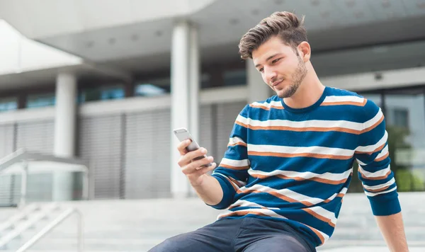 Joven sentado relajado revisando sus mensajes de teléfono inteligente —  Fotos de Stock