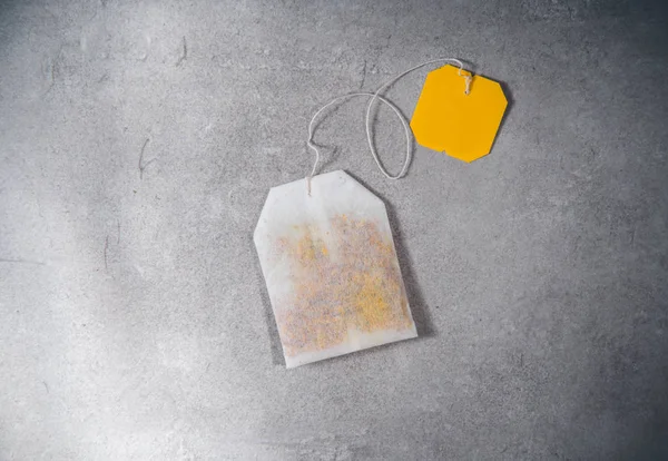 Teabag se žlutým štítkem na šedém stole. Horní pohled na čajový sáček — Stock fotografie
