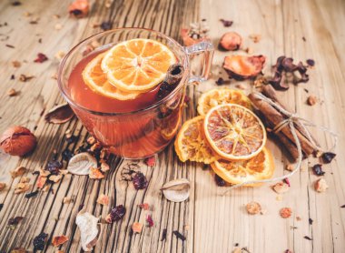 Kuru portakallı bir bardak meyve çayı ve ahşap masada tarçın.